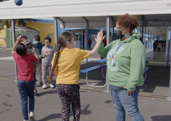 A staff member high-fives students on the yard of The Primary School in the San Francisco Bay Area