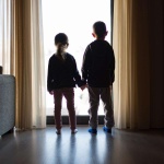 two kids holding hands looking out a window
