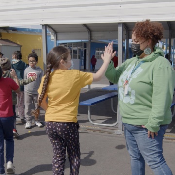 A staff member high-fives students on the yard of The Primary School in the San Francisco Bay Area