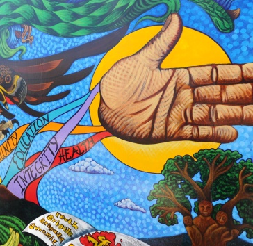A section of a vivid, painted mural showing an outstretched open hand in front of the sun